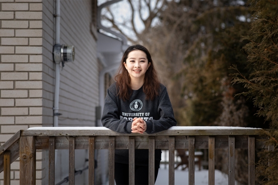 Melody Bagaa smiles as she leans on a snow-covered railing. She wears a University of Toronto sweatshirt.