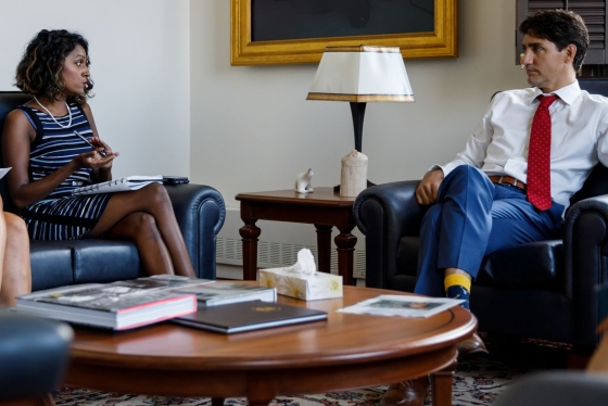 Vandana Fatima Kattar and Justin Trudeau sit in armchairs in an office, next to a table of books and documents.