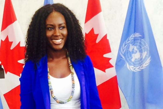 Binta Bajaha standing in front of two Canadian flags and two UN flags