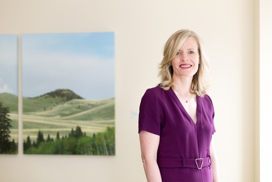 Claire Kennedy smiles as she stands beside a painting of green hills.