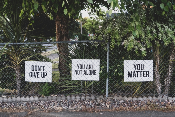 Three signs on a fence read: Don't give up, You are not alone, You matter.