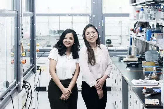 Scientists Nabanita Nawar and Pimyupa Manaswiyoungkul, both wearing white blouses and black pants, stand together in their lab smiling.