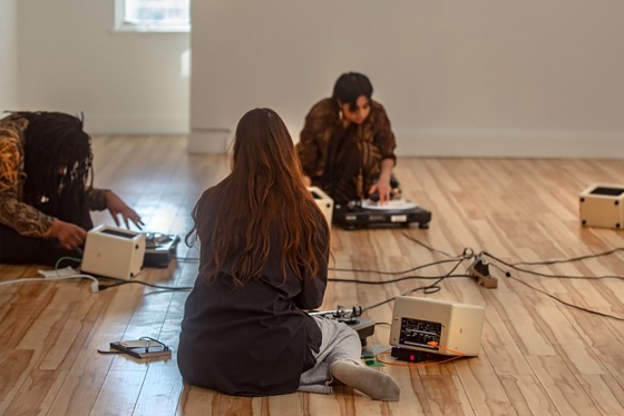 A group of young people sitting on a hardwood floor with some music equipment