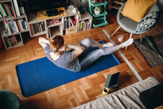 A woman touches her elbow to her knee on a yoga mat on a living room floor.