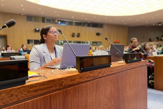 Melanie Ratnam sits at a desk with a microphone in a United Nations assembly room.