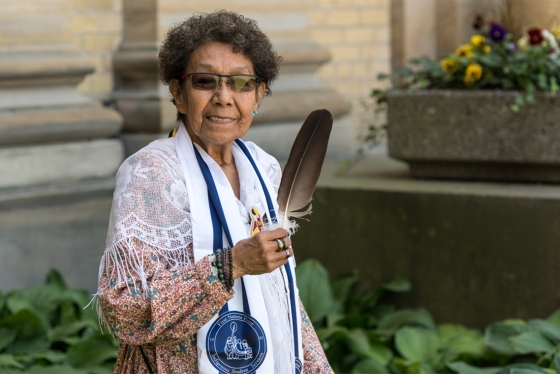 Indigenous elder Jacqueline Lavallee standing outdoors holding a ceremonial eagle feather