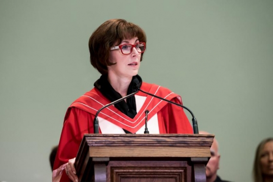 Katie Taylor, wearing academic robes, speaks at a lectern.