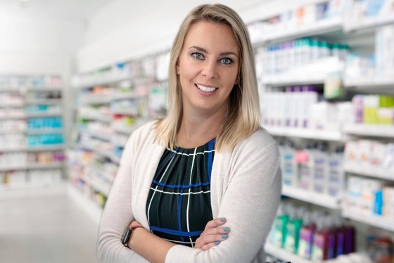 Kristen Watt smiles as she stands in front of pharmacy shelves.
