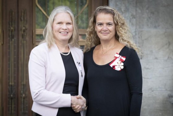 Susan Chatwood and Julie Payette smile as they shake hands. Both women are wearing medals.
