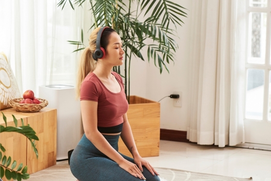A woman wearing headphones kneels on a yoga mat in a living room.