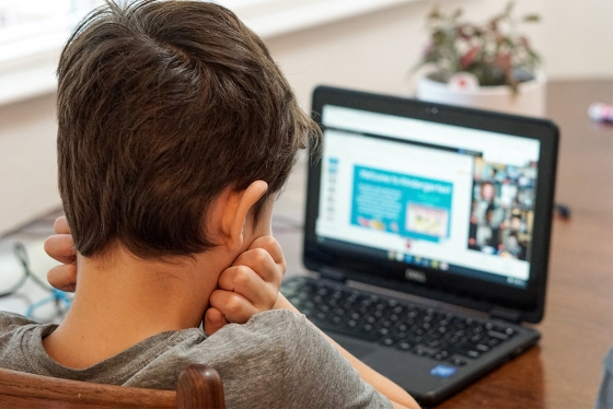 A young boy looks at a laptop screen with his head in his hands.