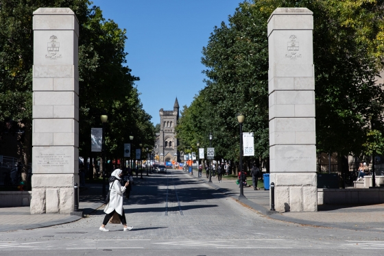 A woman walks past two stone pillars flanking a cobbled street. University College can be seen at the end of the street.