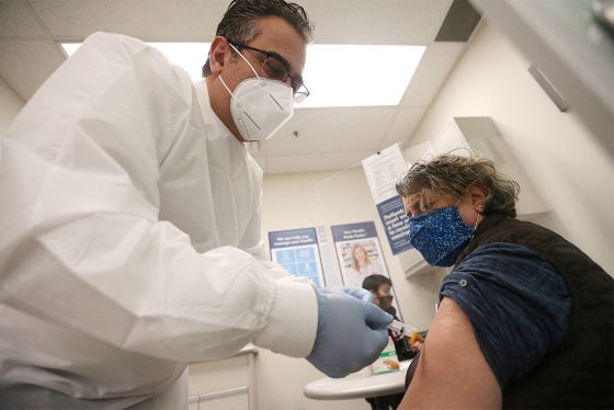 A pharmacist in a mask vaccinates a masked woman in her arm.
