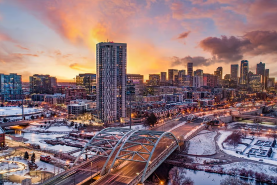 Image of a sunset, with a skyscraper and a bridge with snow on the ground. 