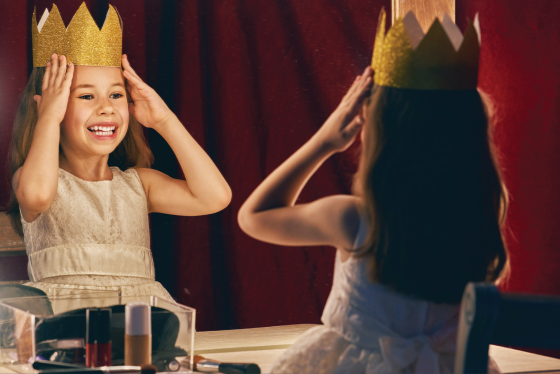 Little girl staring in the mirror putting on a crown