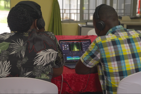 Two men wearing earphones edit a video on a laptop