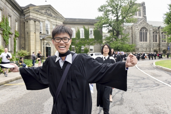 U of T grad in robes with arms outstretched in happiness, grinning at camera