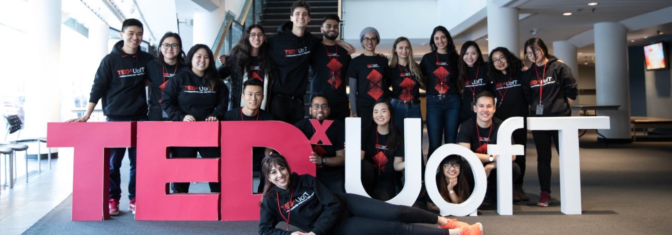 A large group of happy students in matching t-shirts pose with a big sign: TEDx U of T.