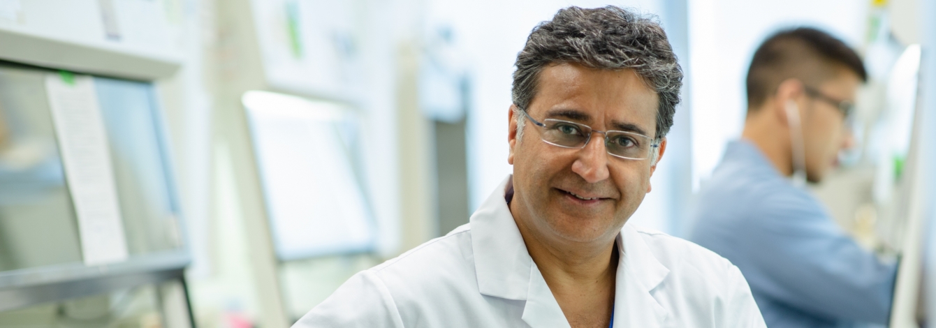 Shaf Keshavjee smiles, wearing a lab coat with the logo: UHN Sprott Surgery
