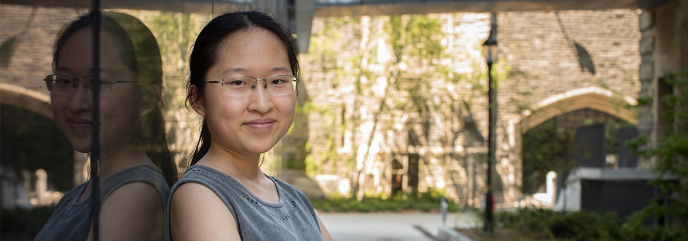 Maddy (Xiaoxiao) Zhang smiles as she leans on a reflecting wall in a sunny courtyard.