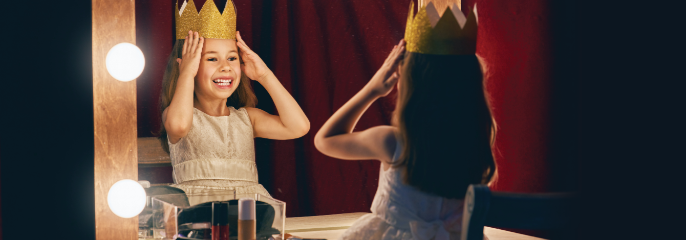 Little girl staring in the mirror putting on a crown