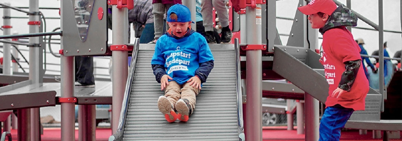 Children play on a slide made of parallel rollers, wearing T-shirts with the Jumpstart logo (photo courtesy of Canadian Tire Jumpstart Charities)