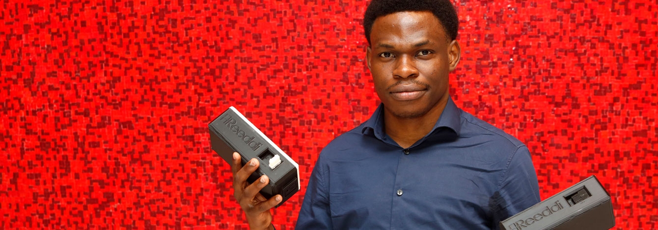 Olugbenga Olubanjo holds up two small rectangular plastic capsules with the Reeddi logo and plug sockets on the end.