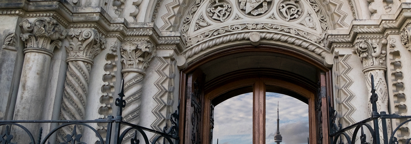 The Toronto skyline with CN Tower is reflected in a door framed by an elaborately carved stone archway.