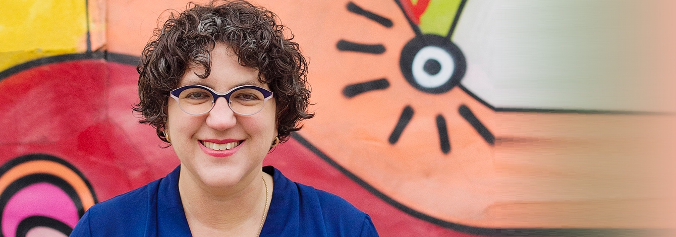 Kady Cowan smiles, standing in front of a vivid hospital wall mural.