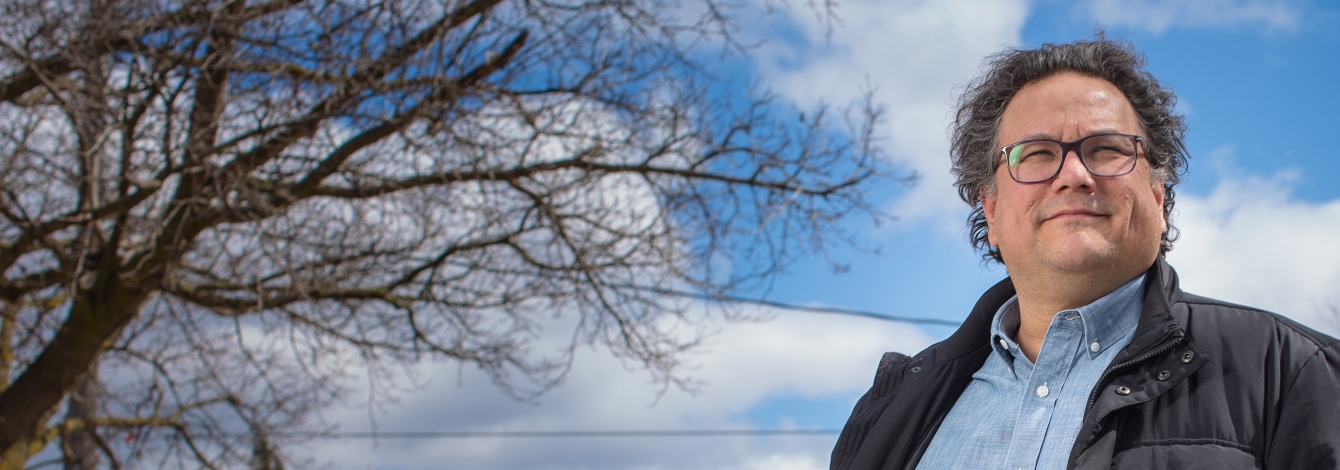 Jesse Wente smiles confidently in front of blue sky and bare tree