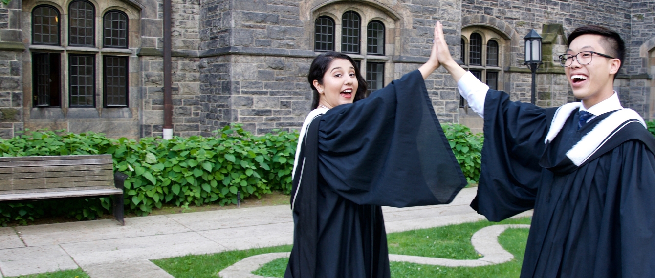 Two recently graduated alumni high-fiving at graduation.