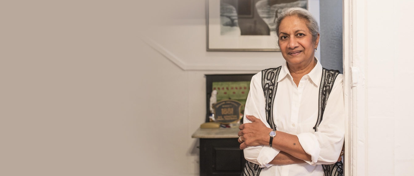 Ceta Ramkhalawansingh leans against a wall inside a home with her arms crossed, smiling.