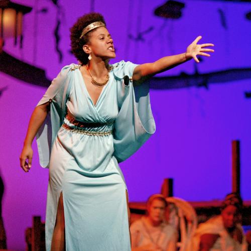 Actress in Grecian gown gesturing passionately on stage at Hart House Theatre