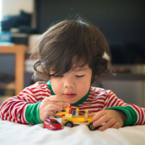 Child playing with a toy truck and car on a bed.