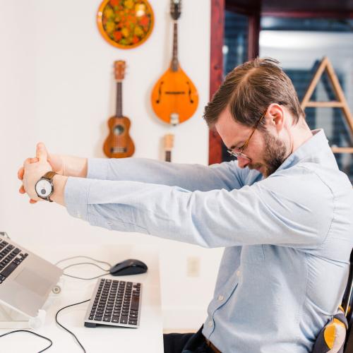 Man sitting at a desk, stretching uncomfortably. 