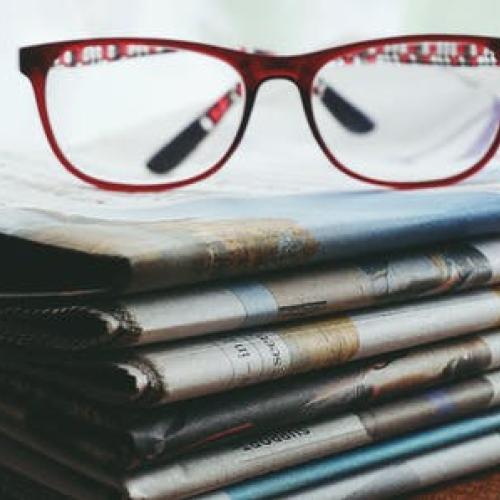 a pair of reading glasses sitting on a stack of newspapers