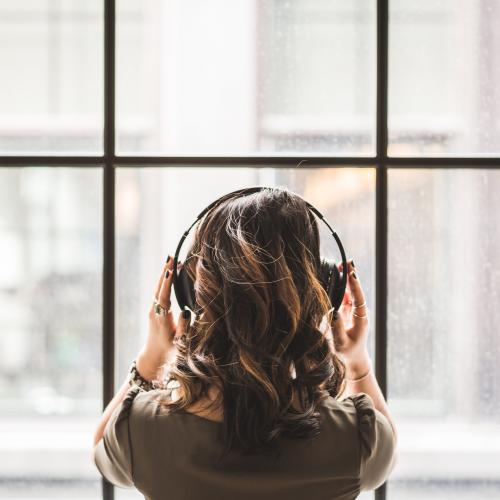 Woman listening to headphones and looking out a wall of windows