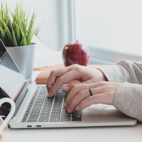 Person in grey sweater sits at desk typing on laptop