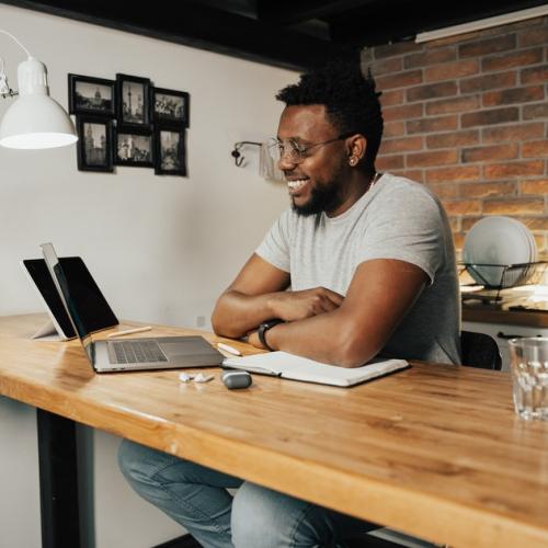 Man in white t-shirt sits at table looking at laptop