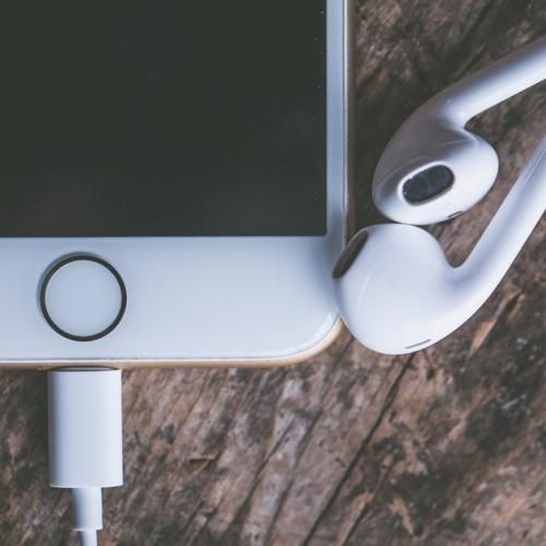 White mobile phone sits with pair of headphones on a table