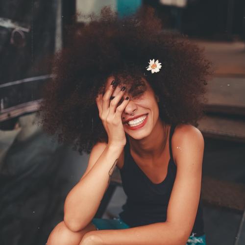 Black woman with curly hair in black sleeve less top  sit smiling on steps