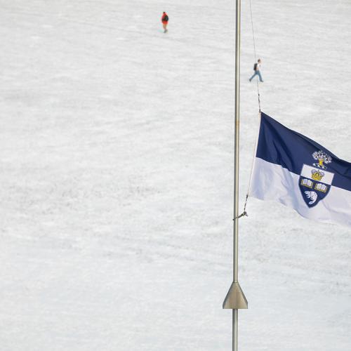 The U of T flag flies at half mast against the background of a snowy campus.