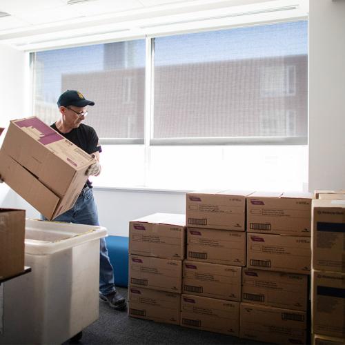 A man lifts a cardboard box and adds it to a large pile of other boxes.