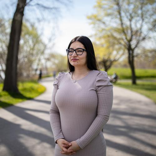 Khadija Hosseini stands on a wooded path by a lake.