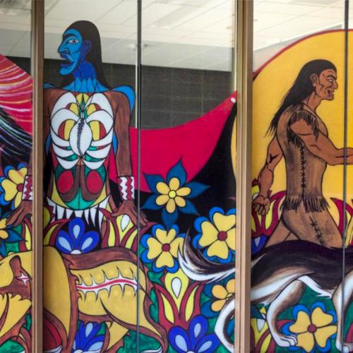 A section of a mural of Indigenous artwork shows a man made of flowers next to stylized bears.