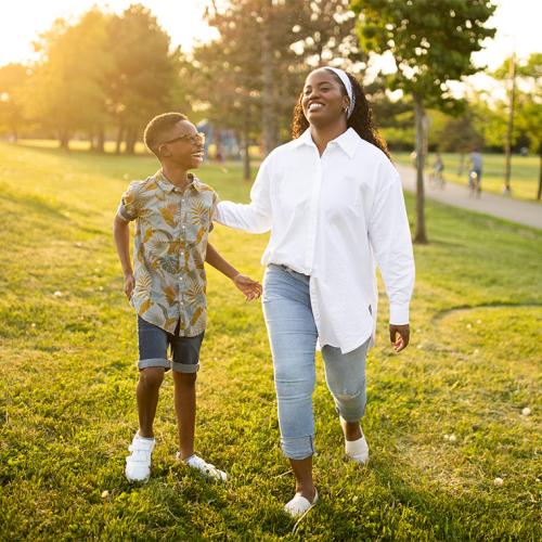 Thereasa Gordon and her young son laugh together, playing on a green hillside at sunset.