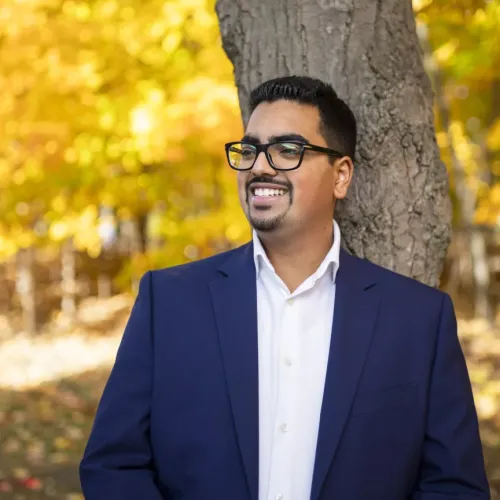 Amit Dalaya in a blue blazer standing under fall trees with yellow leaves