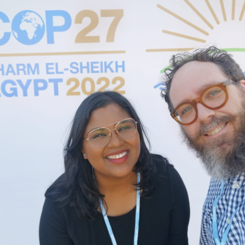 Anjum and a coworker stand in front of a placard, both smiling