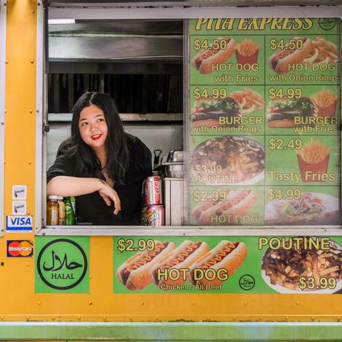 Joanna Luo smiles as she looks out the window of a food truck plastered with prices and images of burgers and fries.