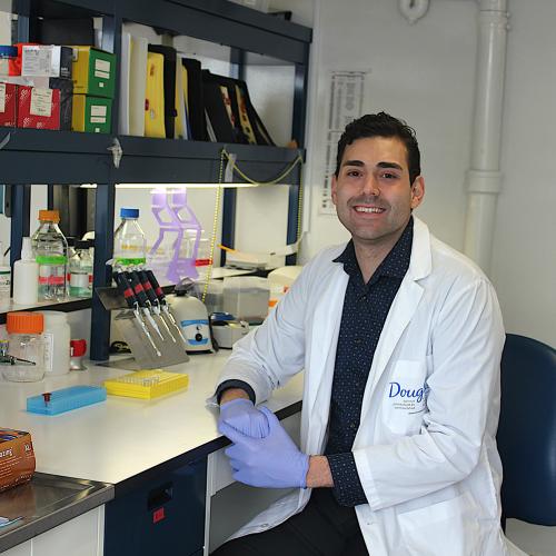 Daniel Almeida smiles as he sits at a lab bench crowded with scientific equipment